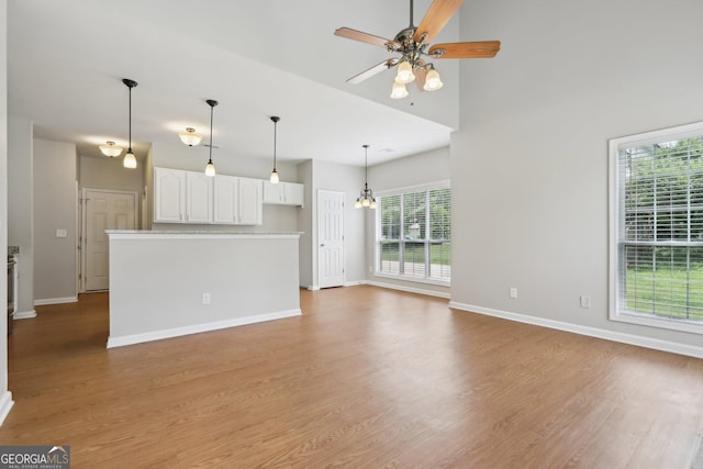 unfurnished living room with healthy amount of natural light, a ceiling fan, wood finished floors, and baseboards