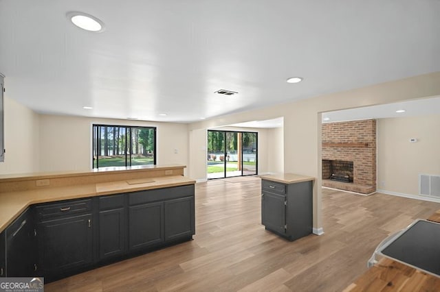 kitchen featuring light wood-style flooring, a peninsula, light countertops, a brick fireplace, and open floor plan