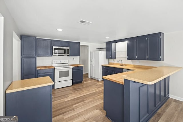 kitchen featuring light wood-style flooring, a sink, blue cabinetry, white appliances, and a peninsula