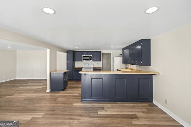 kitchen featuring stainless steel microwave, range with electric cooktop, light countertops, baseboards, and a peninsula