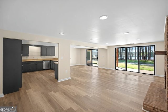 unfurnished living room featuring baseboards, light wood finished floors, recessed lighting, and a sink