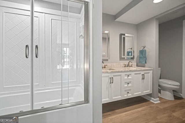 bathroom with a sink, double vanity, combined bath / shower with glass door, toilet, and wood finished floors