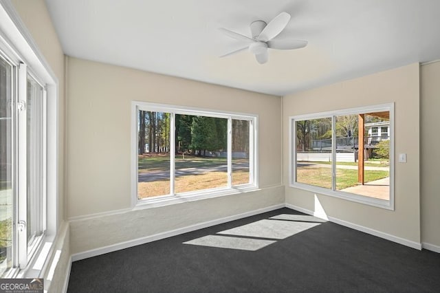 unfurnished room with a ceiling fan, dark carpet, and baseboards