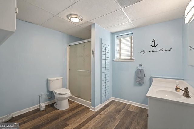 bathroom with a shower stall, vanity, toilet, a drop ceiling, and wood finished floors