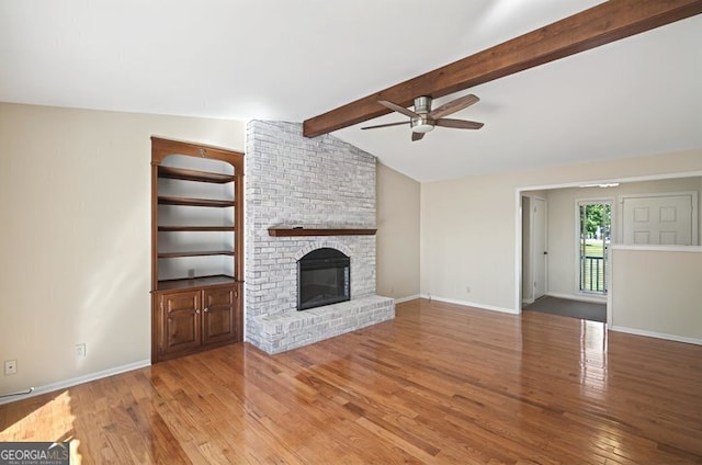 unfurnished living room featuring a brick fireplace, ceiling fan, vaulted ceiling with beams, baseboards, and wood finished floors