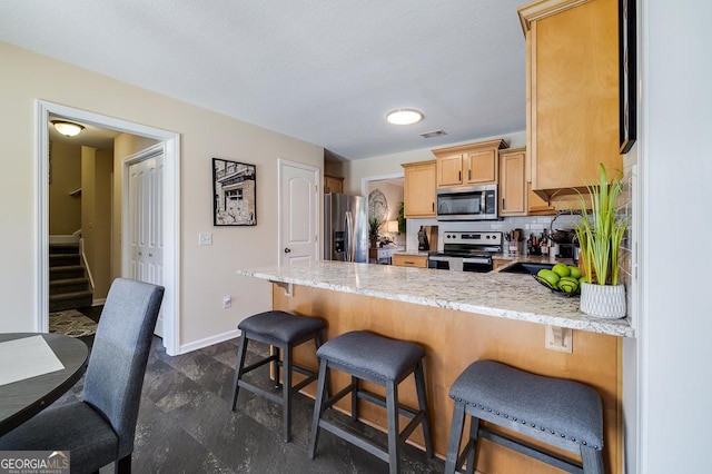 kitchen with visible vents, stainless steel appliances, baseboards, light stone countertops, and a peninsula