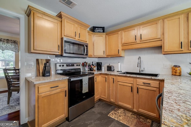 kitchen featuring light stone counters, appliances with stainless steel finishes, backsplash, a sink, and visible vents