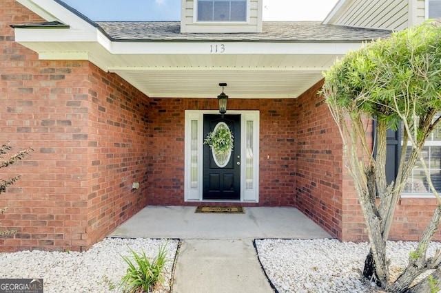 entrance to property featuring roof with shingles, a porch, and brick siding