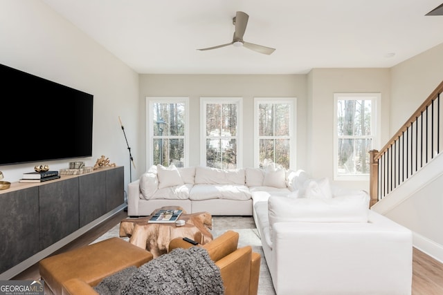 living area with stairway, a wealth of natural light, light wood-style floors, and ceiling fan
