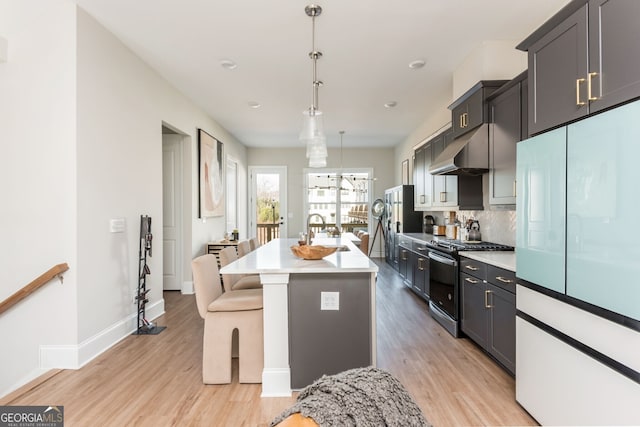 kitchen with light wood-style floors, under cabinet range hood, a sink, white fridge, and range with gas cooktop