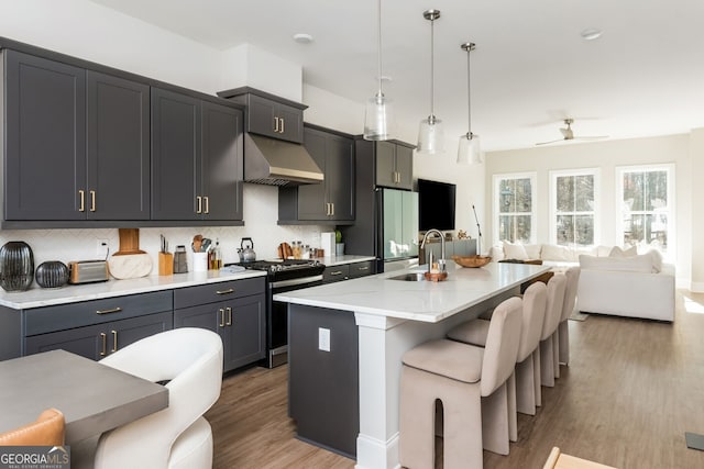 kitchen with light wood finished floors, a sink, under cabinet range hood, stainless steel range with gas cooktop, and open floor plan