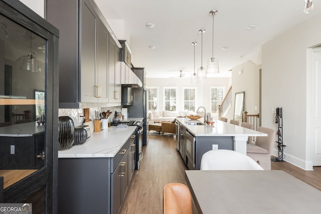 kitchen with wood finished floors, an island with sink, high end stove, a sink, and pendant lighting