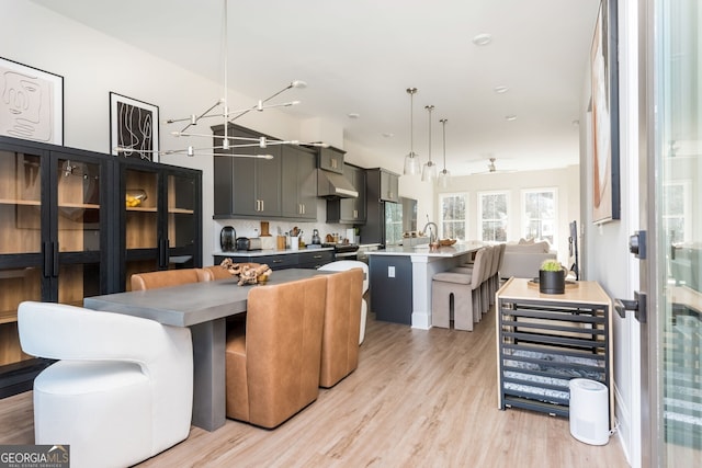 interior space featuring light wood-style flooring, light countertops, under cabinet range hood, a center island with sink, and hanging light fixtures