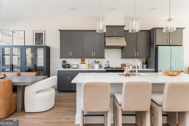 kitchen featuring tasteful backsplash, a sink, under cabinet range hood, decorative light fixtures, and refrigerator