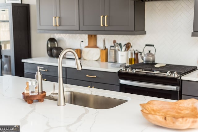 kitchen with gray cabinetry, a sink, stainless steel gas stove, and decorative backsplash