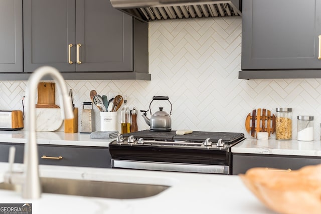kitchen featuring tasteful backsplash, a sink, gray cabinetry, gas stove, and range hood