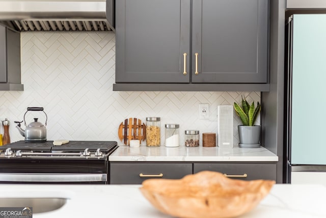 interior space with tasteful backsplash, range hood, freestanding refrigerator, and gas stove
