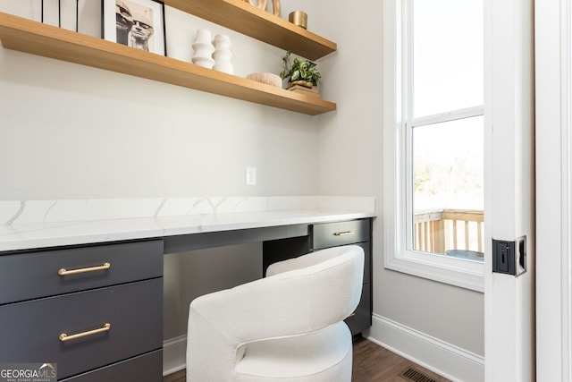 office space featuring dark wood-type flooring, visible vents, built in desk, and baseboards