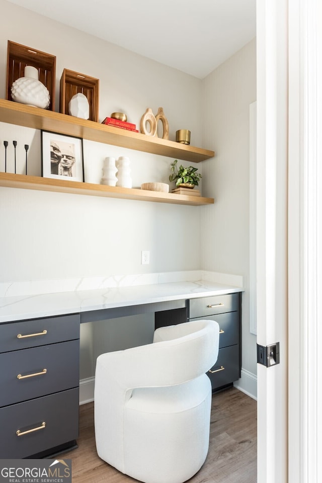 office space featuring light wood-style floors, built in desk, and baseboards