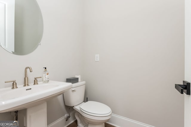 half bathroom featuring a sink, wood finished floors, toilet, and baseboards