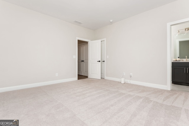 unfurnished bedroom featuring ensuite bath, light colored carpet, a sink, baseboards, and visible vents