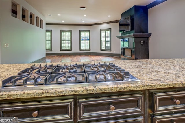kitchen featuring wood finished floors, stainless steel gas cooktop, open floor plan, a fireplace, and ornamental molding