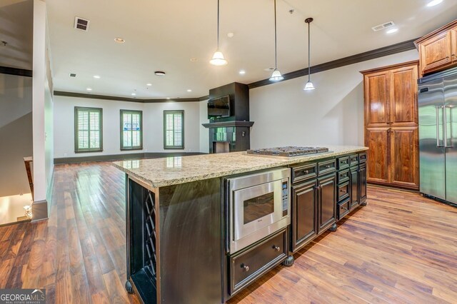 kitchen with light stone countertops, built in appliances, visible vents, and ornamental molding