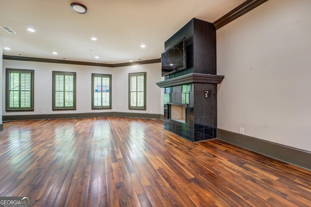 unfurnished living room featuring a fireplace, crown molding, visible vents, baseboards, and wood finished floors