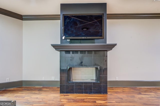 interior details with ornamental molding, a tile fireplace, wood finished floors, and baseboards