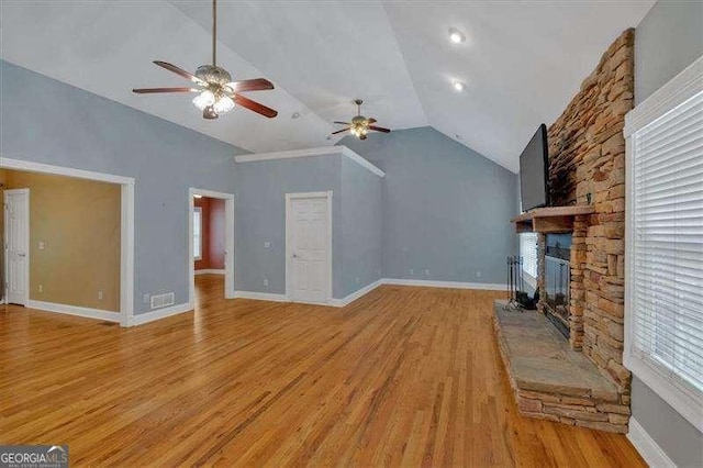 unfurnished living room with a stone fireplace, ceiling fan, light wood finished floors, and vaulted ceiling