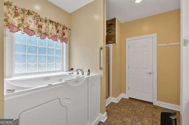 full bathroom featuring a garden tub, a shower stall, and baseboards