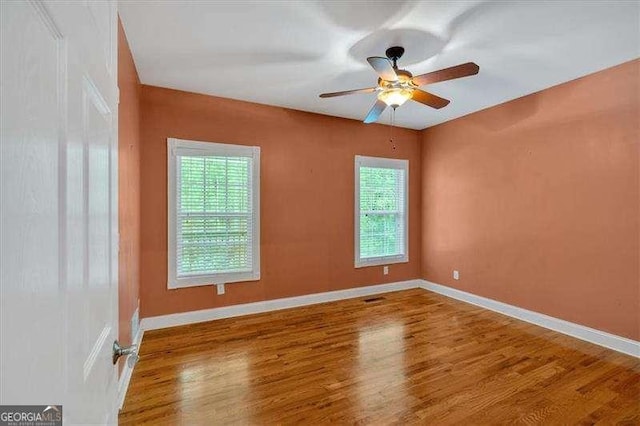 empty room featuring ceiling fan, baseboards, wood finished floors, and a healthy amount of sunlight