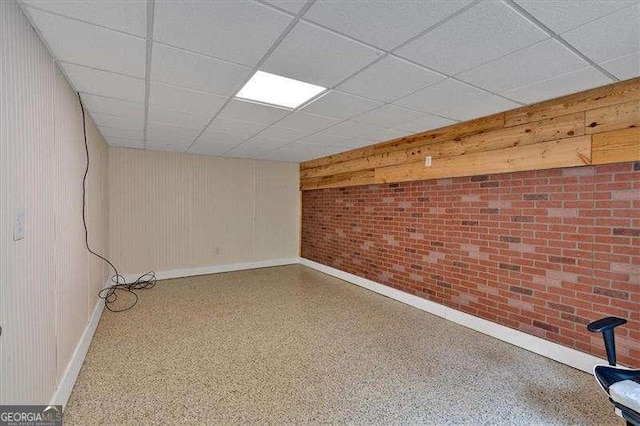 below grade area with brick wall, a paneled ceiling, and baseboards