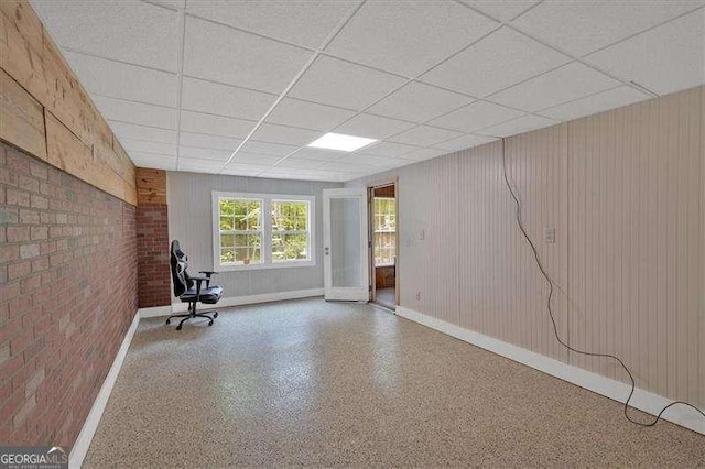 exercise area featuring baseboards, a drop ceiling, and brick wall