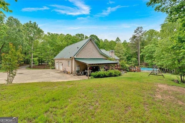 rear view of property featuring a patio area, a forest view, a lawn, driveway, and a chimney
