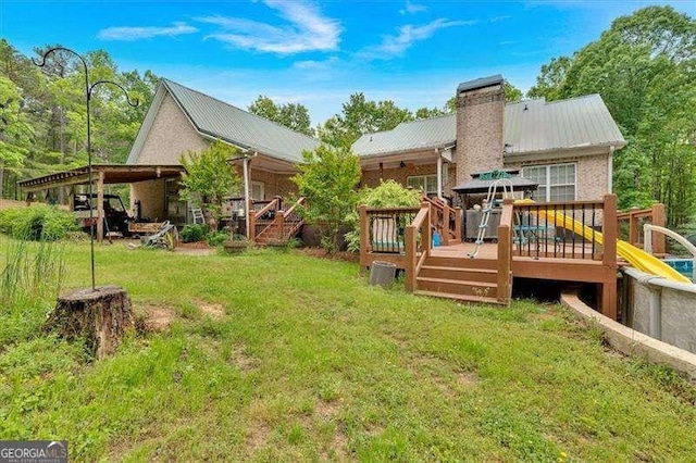 rear view of house with a lawn, a chimney, metal roof, and a wooden deck