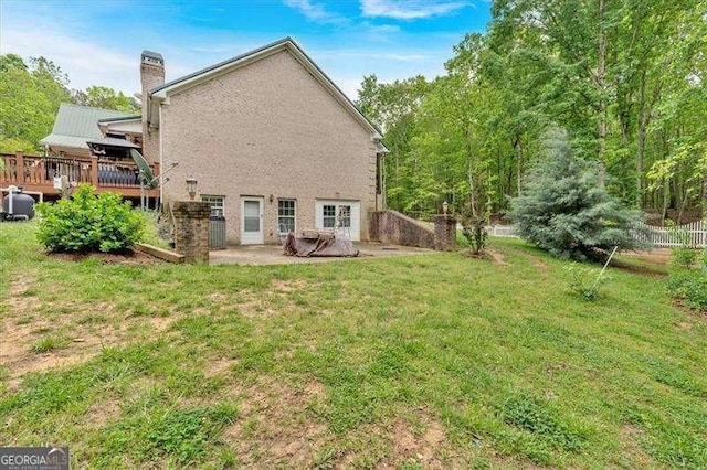 rear view of house with a deck, a chimney, a patio area, and a lawn
