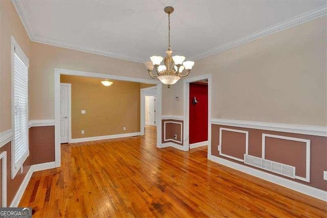unfurnished dining area featuring wood finished floors, a wainscoted wall, visible vents, a notable chandelier, and crown molding