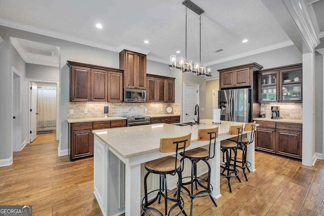 kitchen with a kitchen island with sink, decorative backsplash, a breakfast bar, stainless steel appliances, and light countertops