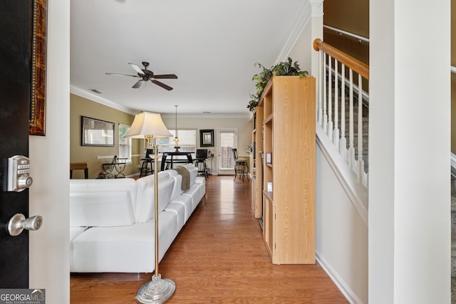 living room featuring stairway, crown molding, a ceiling fan, light wood-style flooring, and baseboards
