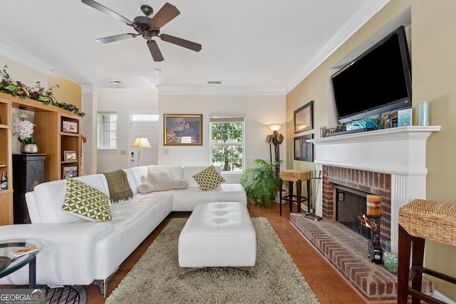 living area with a brick fireplace, a ceiling fan, visible vents, and ornamental molding