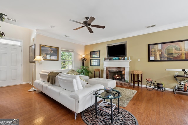 living room with a fireplace, wood finished floors, a ceiling fan, and crown molding