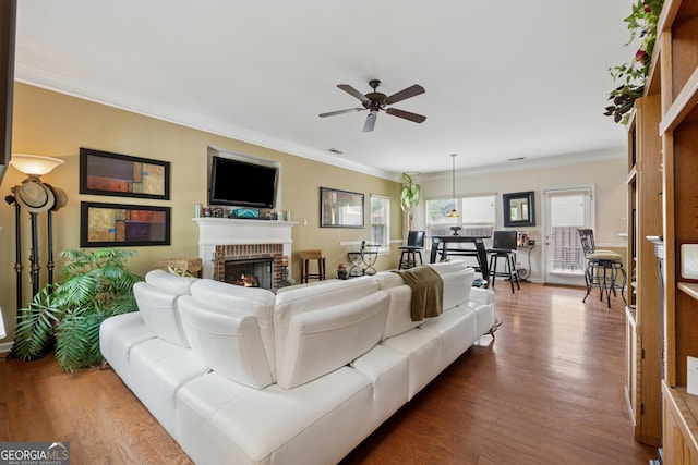 living area with ornamental molding, dark wood-style floors, ceiling fan, and a fireplace