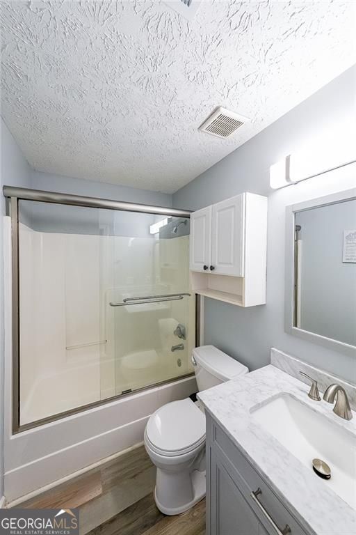 2889 Estuary Dr, Acworth, GA 30101 - bathroom featuring wood finished floors, vanity, a textured ceiling, visible vents, and combined bath / shower with glass door