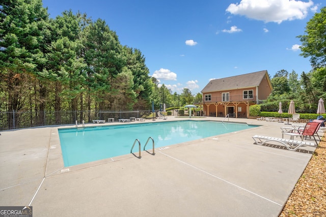 community pool with fence, a patio, and view of wooded area