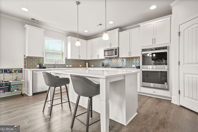 1606 Chancery Ln, Lithia Springs, GA 30122 - kitchen with appliances with stainless steel finishes, wood finished floors, light countertops, a breakfast bar area, and crown molding