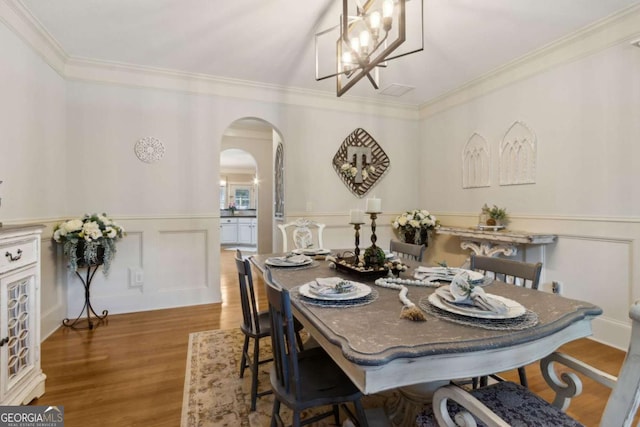 dining space with crown molding, arched walkways, a chandelier, and wood finished floors