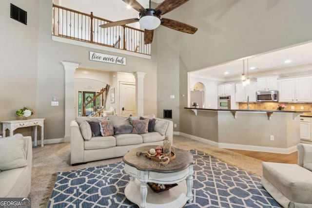 living room featuring ornate columns, stairway, ceiling fan, visible vents, and baseboards