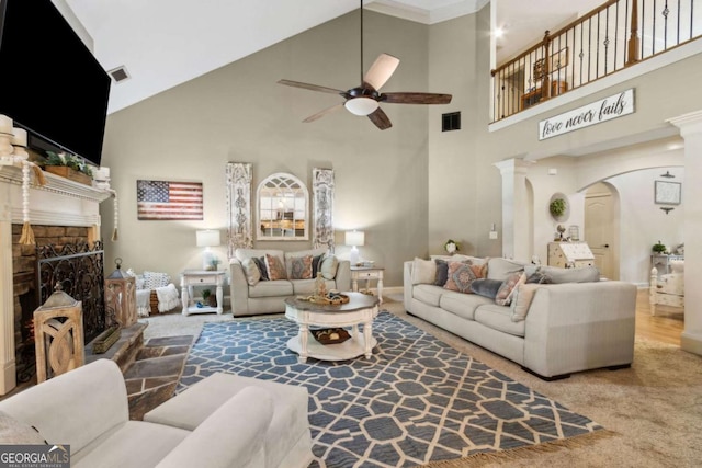 carpeted living area featuring a fireplace with raised hearth, a ceiling fan, visible vents, a towering ceiling, and arched walkways