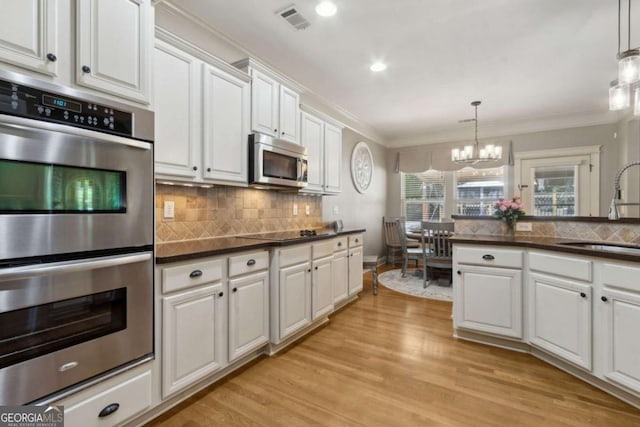kitchen featuring stainless steel appliances, dark countertops, light wood finished floors, a sink, and visible vents